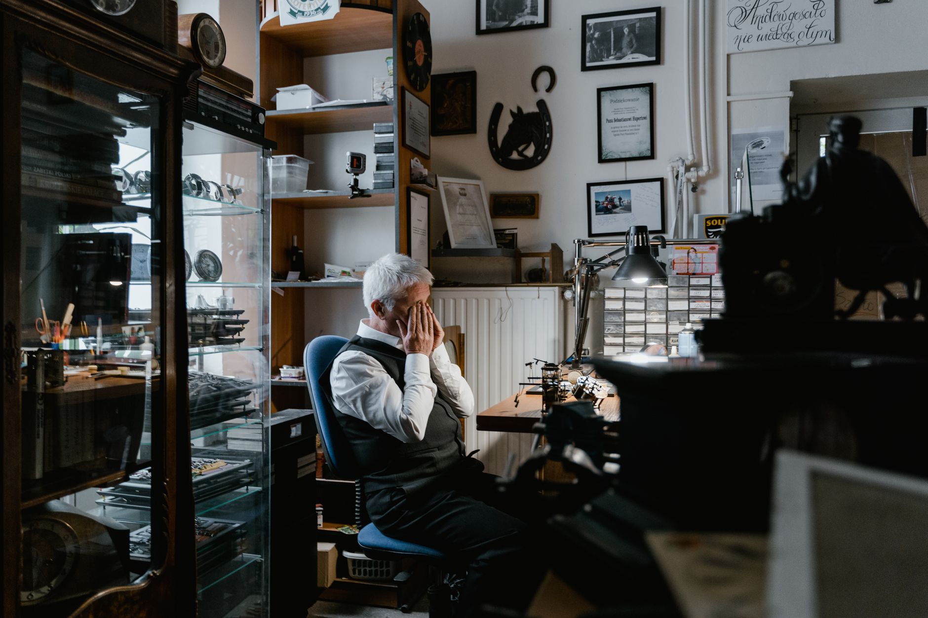 A tired man rubbing his eyes at a cluttered desk piled with paperwork