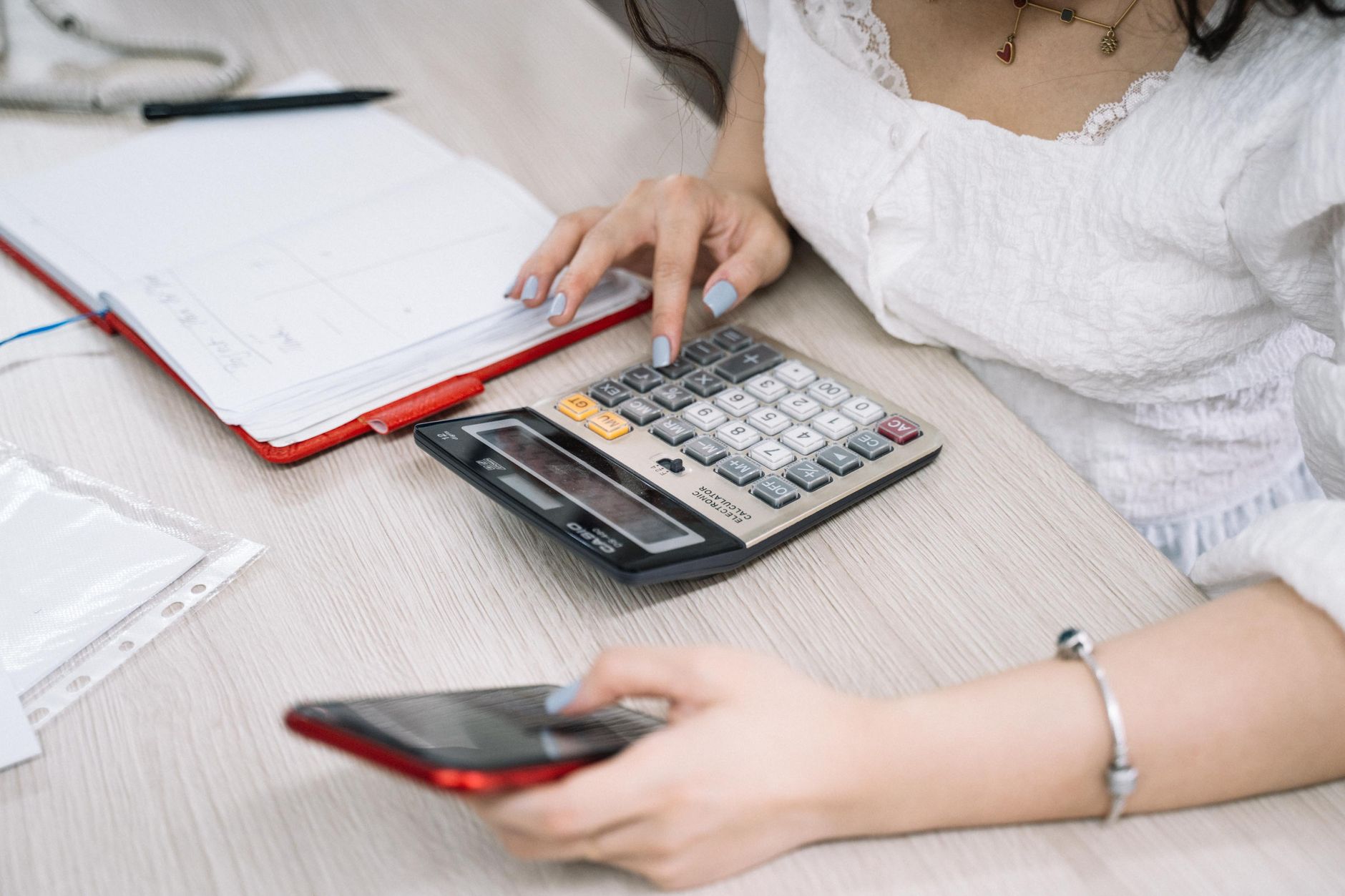 A business owner reviews monthly enquiry figures with a calculator and a handwritten notebook, working out her conversion rate.