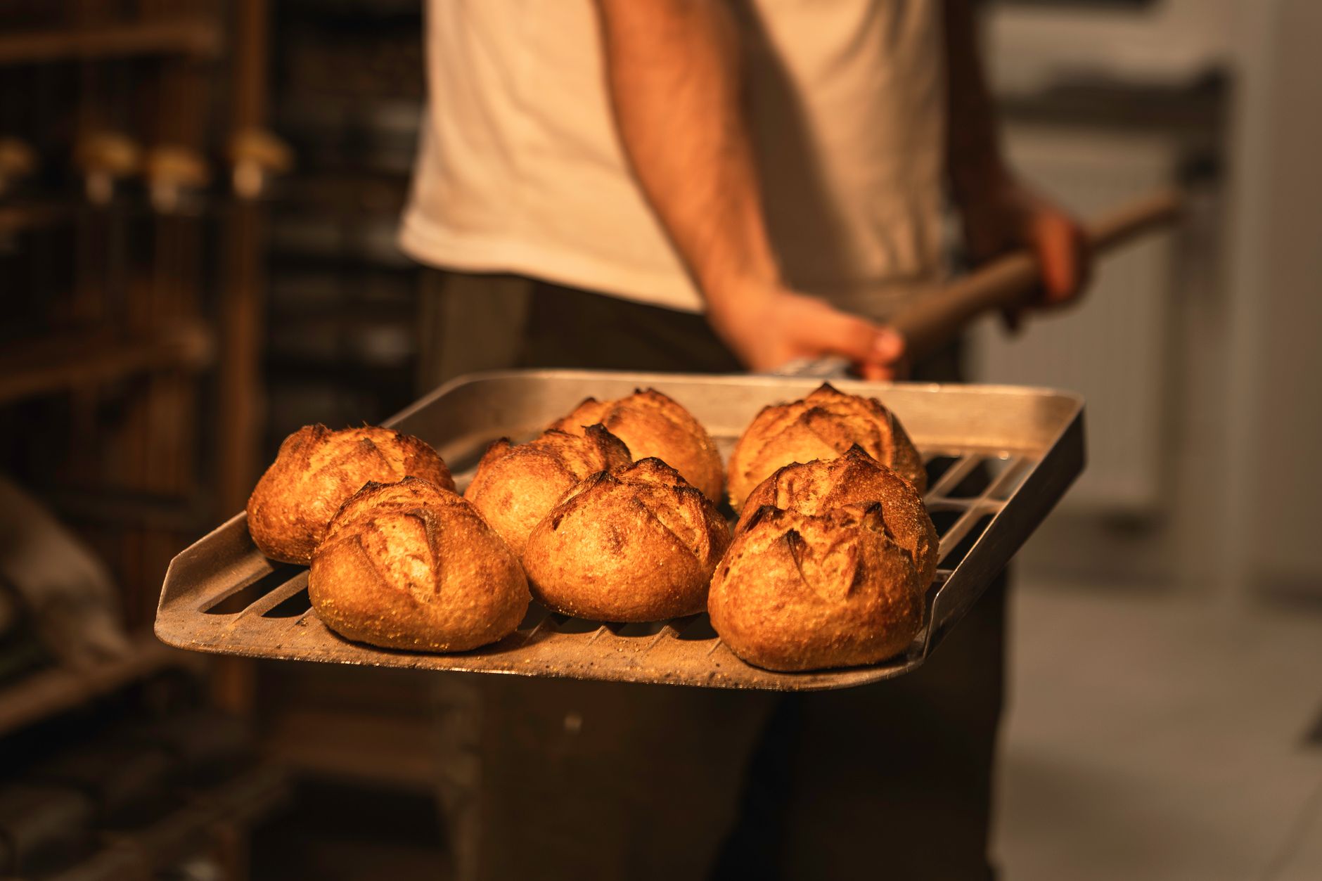A baker pulling a fresh loaf of sourdough from the oven